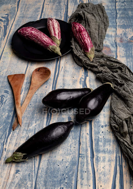 Fresh ripe eggplants near piece of striped cloth on weathered wooden tabletop — Stock Photo