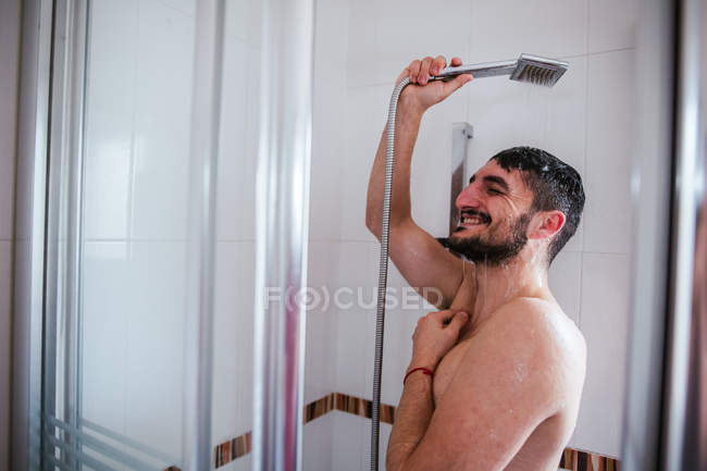 Без рубашки улыбающийся мужчина принимает душ в ванной комнате — стоковое фото