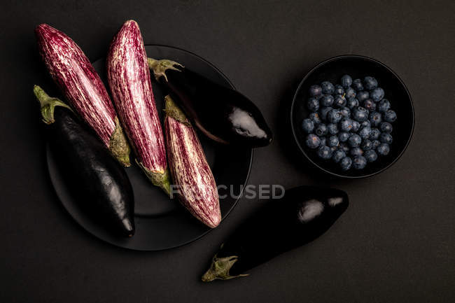 Fresh ripe eggplants and blueberries in bowl on black table — Stock Photo