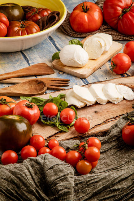 Tomates fraîches et fromage mozzarella aux feuilles de basilic pour salade sur planche et tissu en bois — Photo de stock