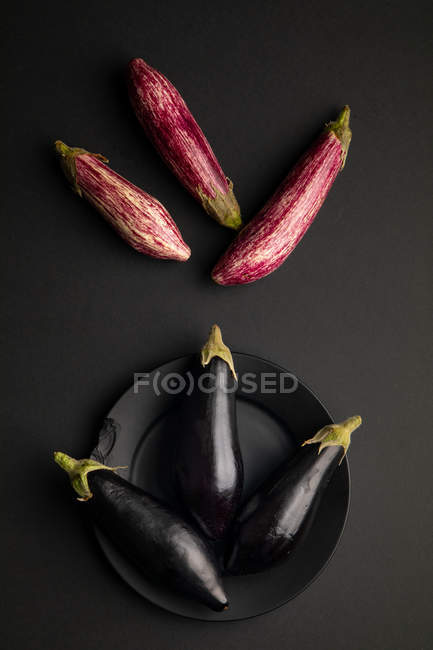 Set frischer reifer Auberginen mit Teller auf schwarzem Tisch — Stockfoto