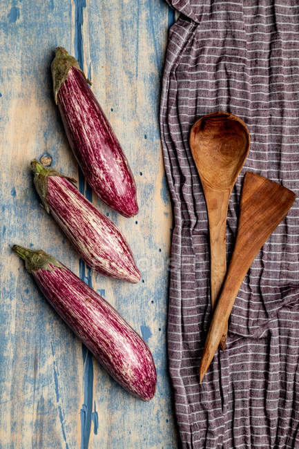 Fresh ripe eggplants near piece of striped cloth on weathered wooden tabletop — Stock Photo