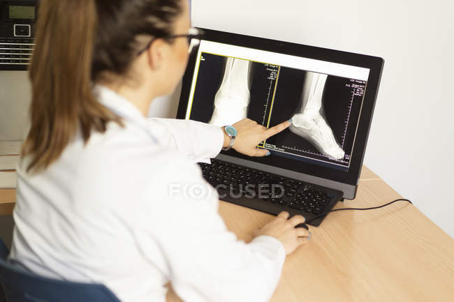 Junge Ärztin in Uniform betrachtet Röntgenbild an Wand im Zimmer — Stockfoto