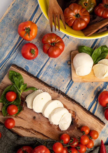 Tomates frescos y queso mozzarella con hojas de albahaca para ensalada sobre tabla y tela de madera - foto de stock
