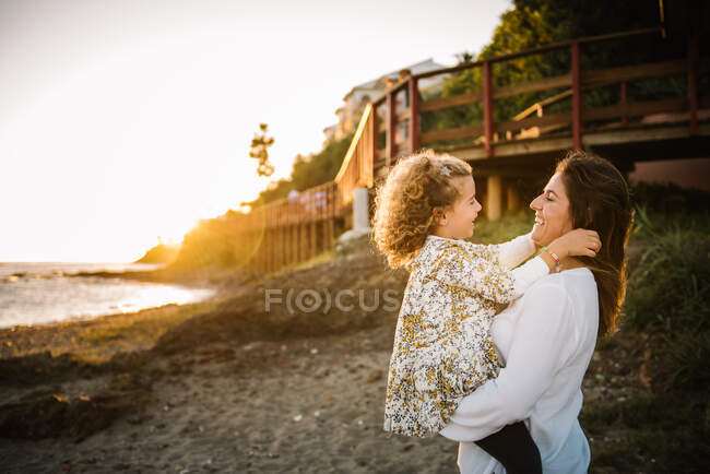 Жінка середнього віку з дочкою на морському березі посміхається і обіймає один одного — стокове фото