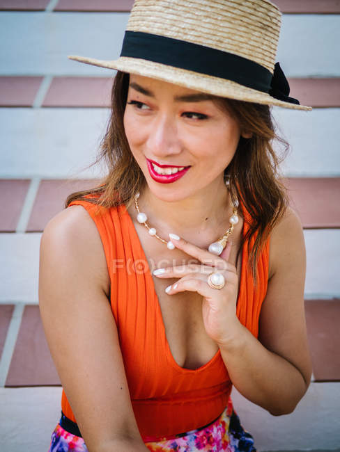 Молодая стильная китаянка в панамской шляпе и солнцезащитных очках сидит на лестнице и наслаждается ярким летним днем — стоковое фото