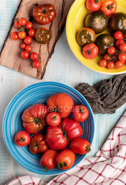 Table en bois avec bols de tomates rouges fraîches assorties — Photo de stock