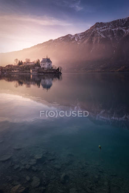 Landschaft des ruhigen blauen Sees mit Häusern am Ufer bei Sonnenuntergang vor dem Hintergrund der Berge in der Sonne, Schweiz — Stockfoto