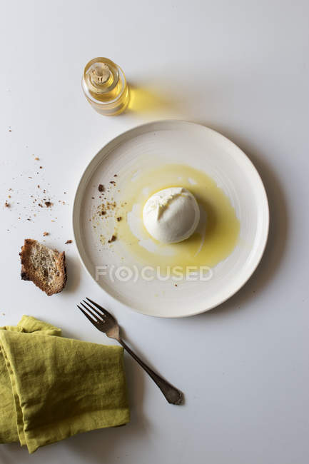Assiette avec une délicieuse burrata fraîche sur une table blanche près du morceau de pain et de l'huile avec du sel — Photo de stock
