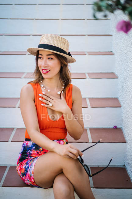 Молода класна жінка в панамському капелюсі і сонячні окуляри сидять на сходах і насолоджуються яскравим літнім днем. — стокове фото
