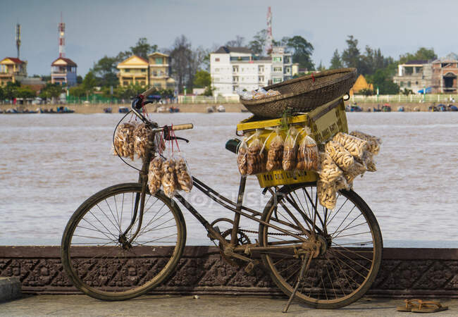 Vieux vélo rouillé avec des poches de nourriture en plastique suspendues et une boîte contre le bord de mer de la ville, Cambodge — Photo de stock