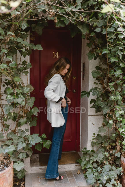 Stylische Frau steht vor roter Tür — Stockfoto
