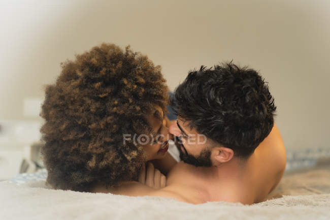 Young man and woman lying on bed and cuddling in cozy room at home — Stock Photo