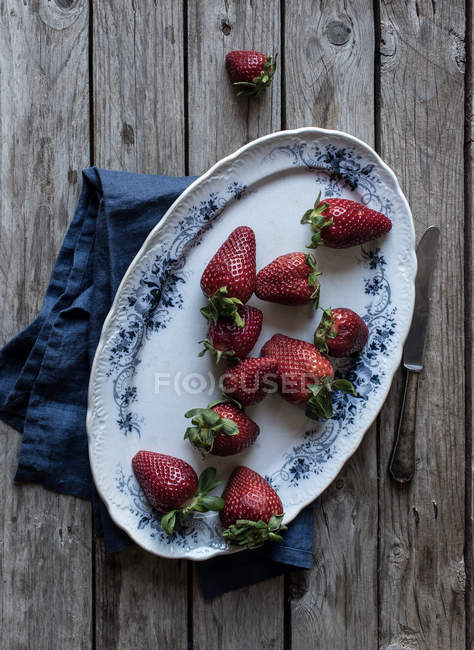 Assiette de délicieuses fraises mûres sur table en bois près de serviette bleue et couteau en métal — Photo de stock