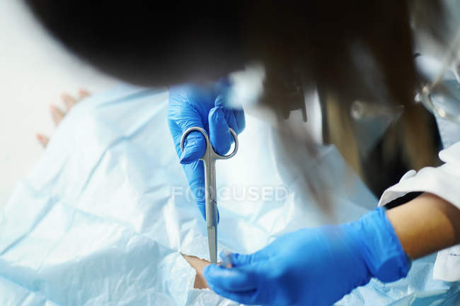 Female doctor in uniform and medical mask taking out stitches from crop hand of patient in napkin — Stock Photo