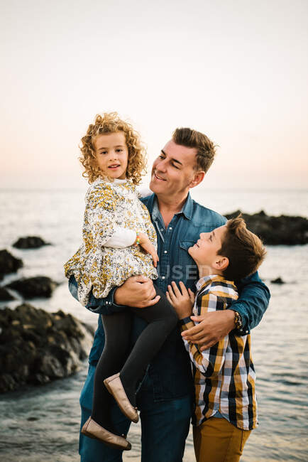 Uomo di mezza età con i suoi figli sulla riva del mare sorridendo e abbracciandosi — Foto stock
