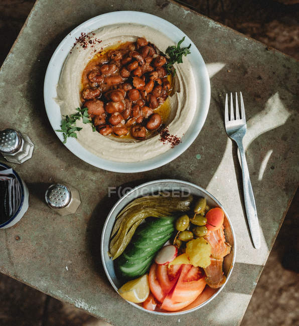 Haricots et houmous traditionnels dans une assiette avec légumes en pot sur une table en bois — Photo de stock