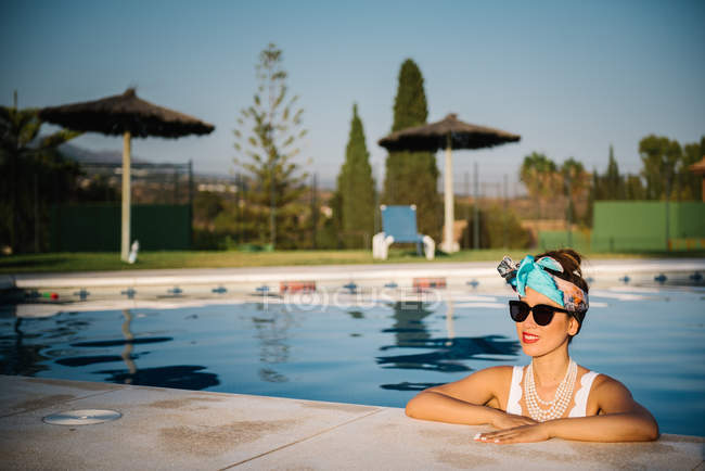 Joven mujer china rica tomando el sol junto a una piscina en un complejo de lujo - foto de stock
