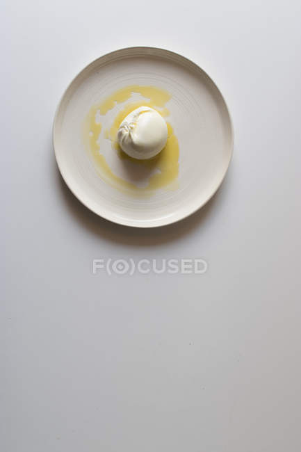 Шар вкусной бурраты с маслом на керамической пластине на белом фоне — стоковое фото
