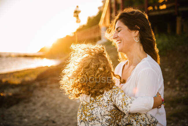 Mulher de meia idade com sua filha na costa do mar sorrindo e abraçando uns aos outros — Fotografia de Stock