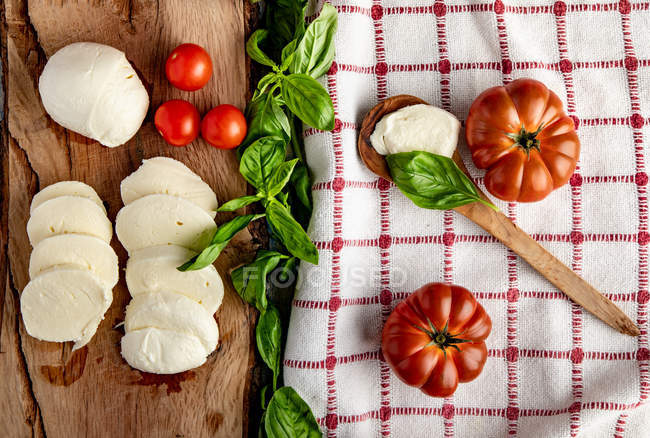 Tomates frescos e queijo mussarela fatiado com folhas de manjericão para salada em tábua de madeira e guardanapo de tecido — Fotografia de Stock
