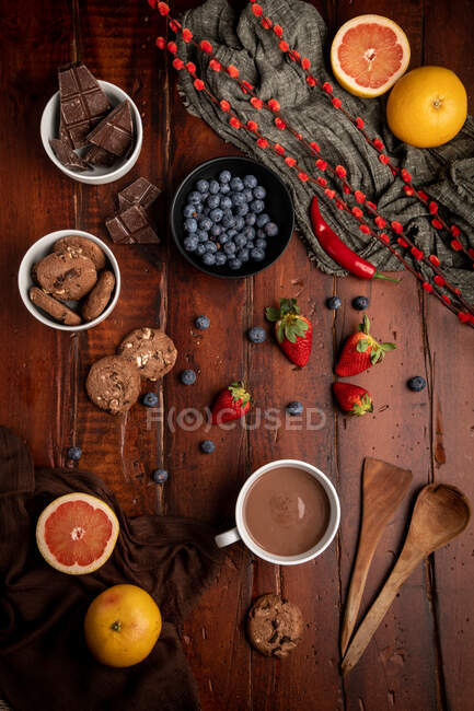 Becher mit leckerer heißer Schokolade auf Holztisch in der Nähe von verschiedenen Desserts und Früchten zum Frühstück — Stockfoto