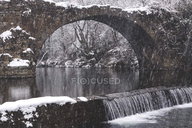 Fluss fließt im verschneiten Winterwald mit alter zerstörter Brücke — Stockfoto