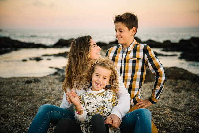 Donna di mezza età con i suoi figli sulla riva del mare sorridenti e che si abbracciano — Foto stock