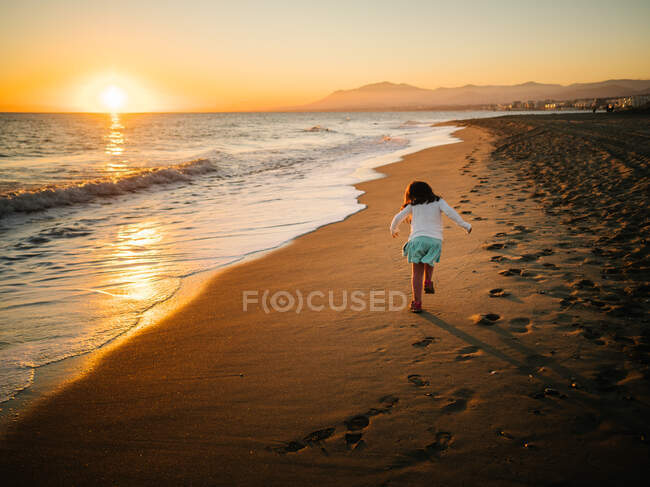Back view of anonymous little girl running sand at beach — Stock Photo