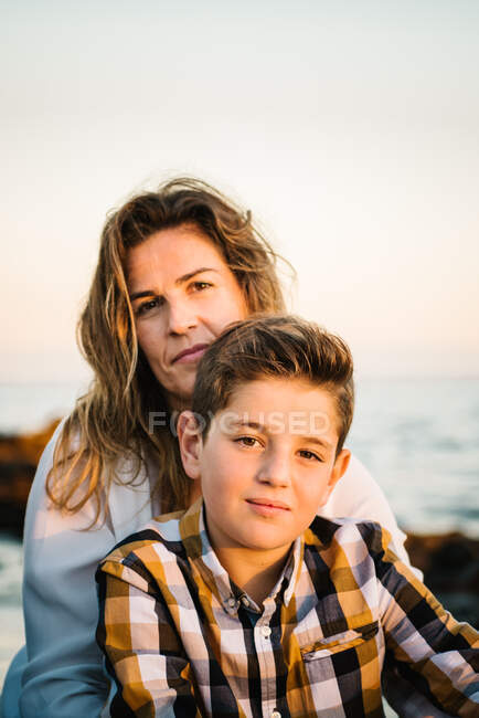 Donna di mezza età con suo figlio sulla riva del mare che sorride e si abbraccia — Foto stock