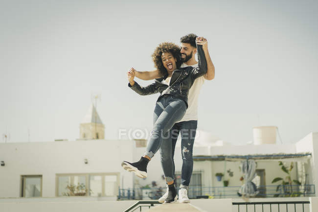 Multiracial man and woman laughing and balancing on wall while having fun on city street during date — Stock Photo