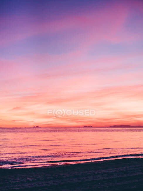 Vue de la côte au coucher du soleil violet dans un ciel nuageux sur l'océan. — Photo de stock