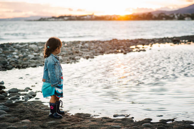 Menina irreconhecível em pé à beira-mar ao pôr-do-sol — Fotografia de Stock