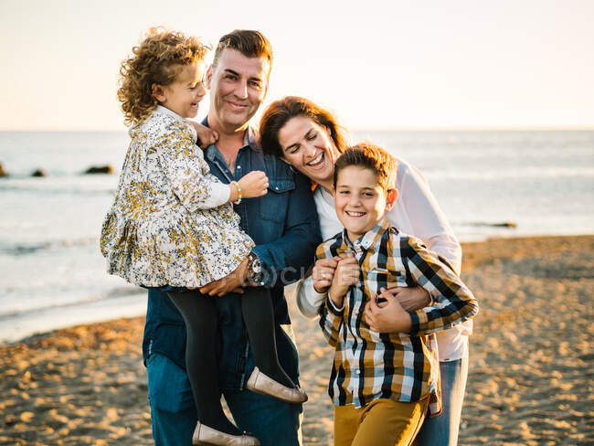 Homem de meia idade uma mulher com filhos na costa do mar sorrindo e abraçando uns aos outros — Fotografia de Stock