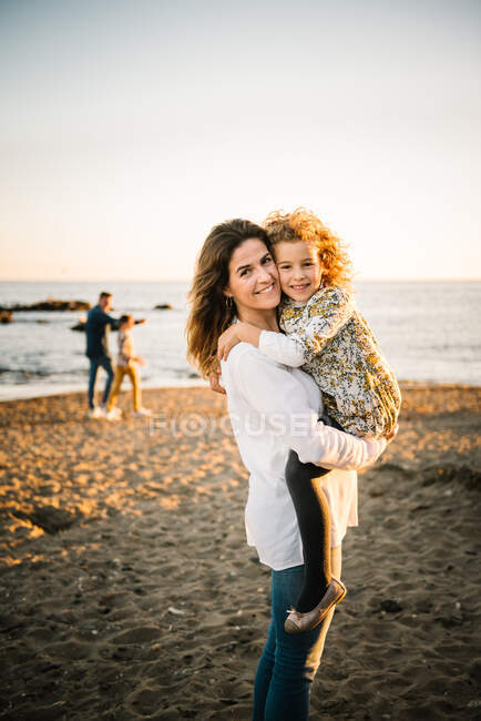 Mujer de mediana edad con su hija en la orilla del mar sonriendo y abrazándose - foto de stock