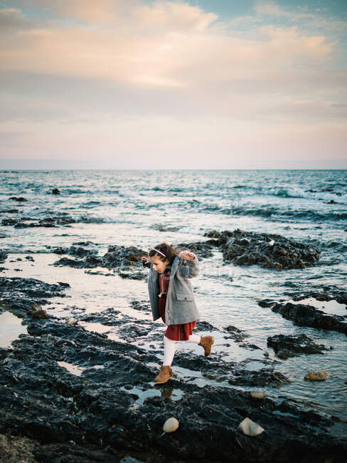Kleines Mädchen, das an einem Wintertag am Strand auf Felsen spaziert — Stockfoto