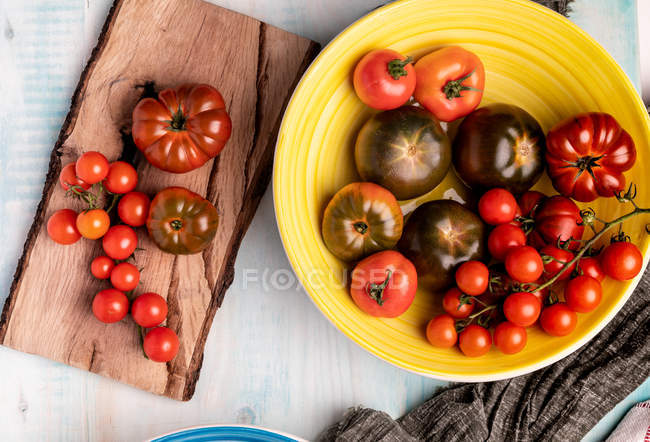 Mesa de madeira com tigela de tomates vermelhos frescos sortidos — Fotografia de Stock