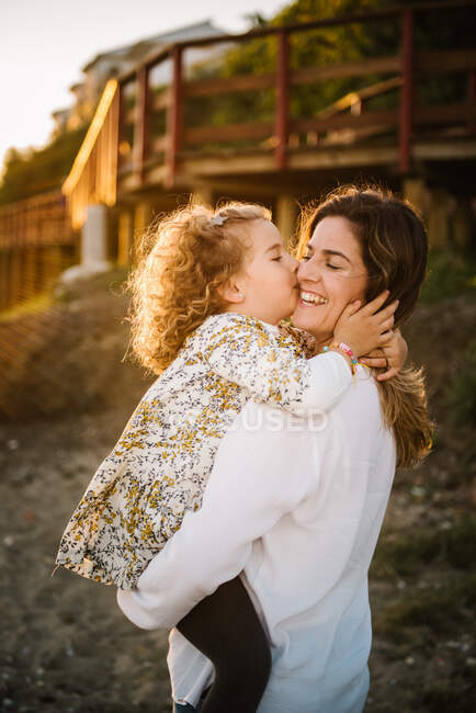 Женщина средних лет с дочерью на берегу моря улыбаются и обнимают друг друга — стоковое фото