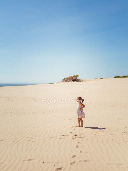 Nettes kleines Mädchen steht an einem strahlenden Sommertag auf einer Sanddüne — Stockfoto