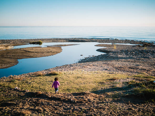 Rückansicht eines nicht wiederzuerkennenden Mädchens, das bei Sonnenuntergang am Ufer des Meeres spaziert — Stockfoto