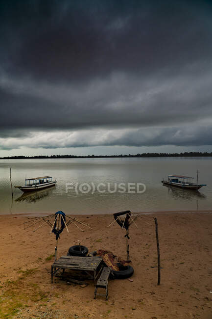 Barcos tradicionales en la playa de arena con aguas tranquilas bajo el cielo nublado oscuro, Camboya - foto de stock