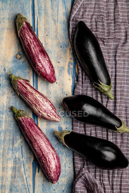 Set of fresh ripe purple and black eggplants near piece of striped cloth on weathered wooden tabletop — Stock Photo