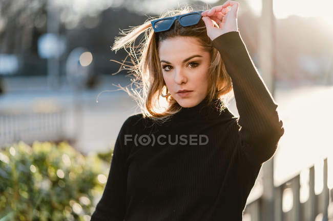 Stylish young girl taking off sunglasses on sunny street — Stock Photo