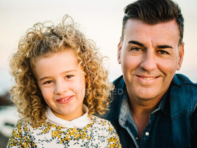 Чоловік середнього віку з дочкою на морському березі посміхається і обіймає один одного — стокове фото