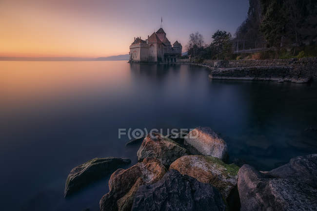 Farbenfroher Sonnenuntergangshimmel über dem ruhigen See mit Felsen und Festung am Ufer, Schweiz — Stockfoto