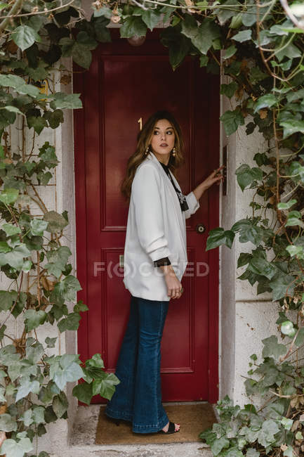 Donna elegante in piedi vicino alla porta rossa — Foto stock