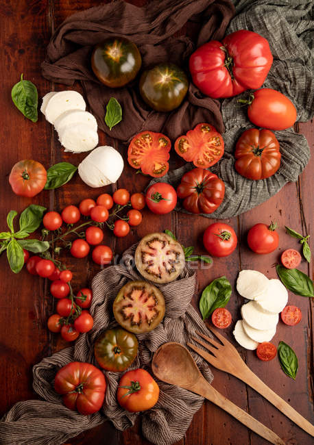 Pomodori freschi e mozzarella con foglie di basilico per insalata sul tavolo di legno — Foto stock