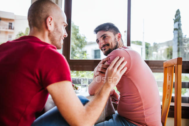 Affectionate gay couple flirting at table in kitchen — Stock Photo