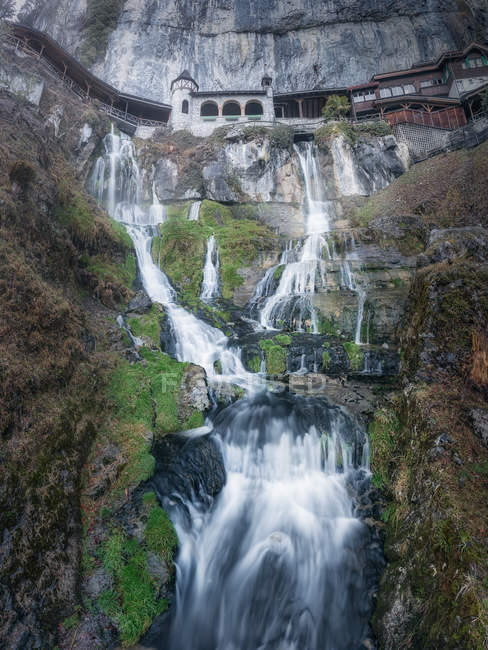Water cascade falling from rocky cliff with building above, Switzerland — Stock Photo