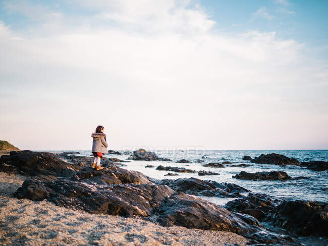 Anonymes kleines Mädchen von hinten, das am Strand auf Sand steht und auf das Meer blickt — Stockfoto